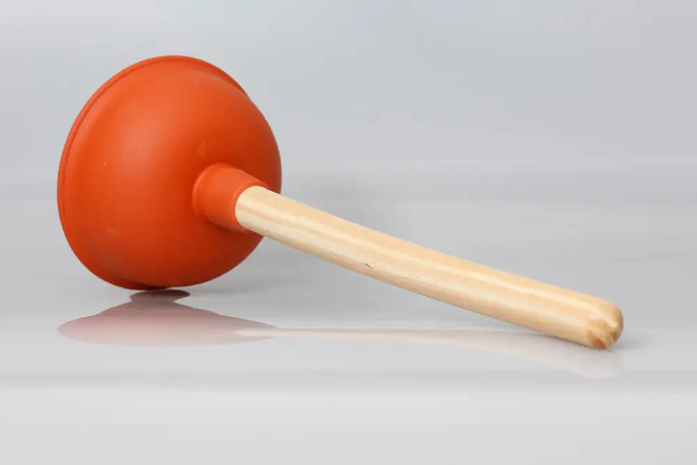 Desatascador de ventosa con la copa de goma naranja y el mango de madera, sobre un fondo blanco