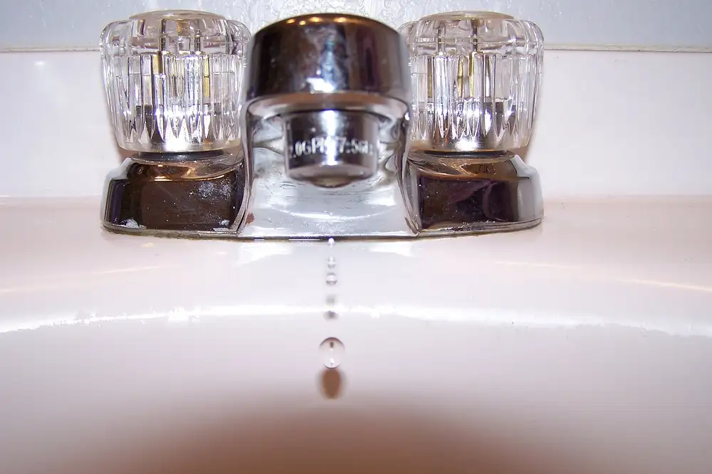 Grifo de lavabo cromado con dos mandos transparentes y una gota de agua cayendo del caño