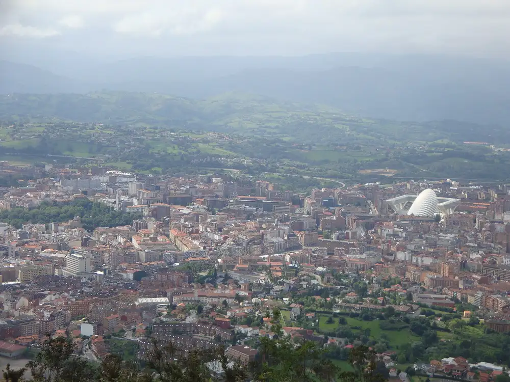 Vista de Oviedo desde el monte Naranco, con el casco urbano, el edificio blanco del Palacio de Congresos y montes verdes al fondo