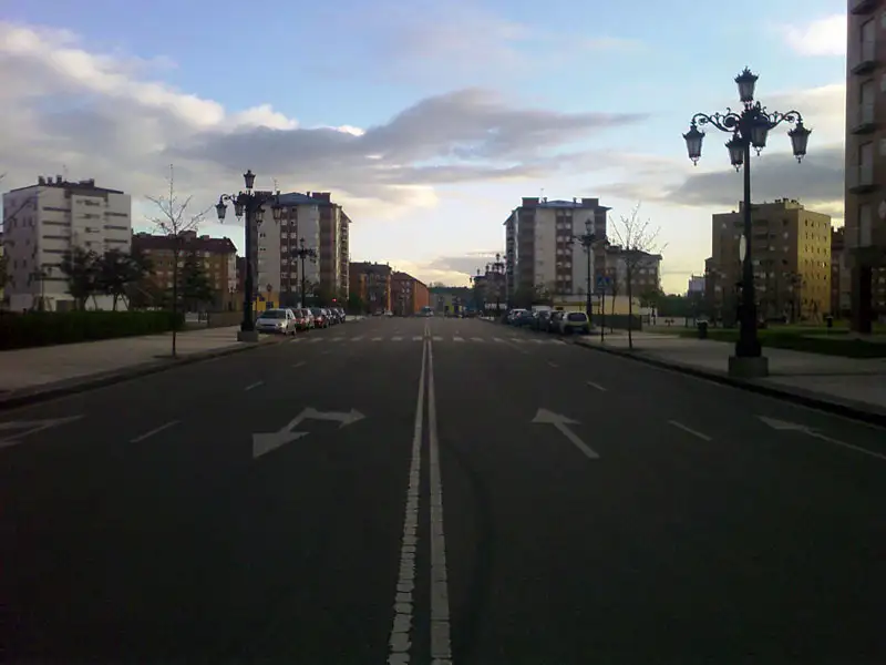 Avenida ancha con farolas y bloques de viviendas de varias plantas a los lados en La Corredoria, al atardecer
